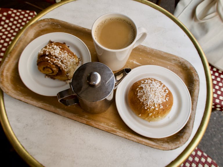 Enjoy a warm cup of coffee with cinnamon roll and bun on a cozy Helsinki café table.